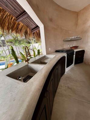 A kitchen with a large island, a built-in oven, and a view of a pool and tropical plants. - Quaint 3-bedroom house with WiFi in Troncones (Troncones)