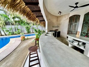 A modern kitchen with a built-in island, a pool, and a thatched roof. - Quaint 3-bedroom house with WiFi in Troncones (Troncones)