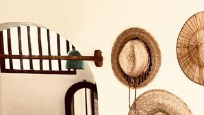 Ein Zimmer mit einer Holzbank, einem kleinen Waschbecken und einem Spiegel. Drei gewebte Hüte hängen an der Wand.