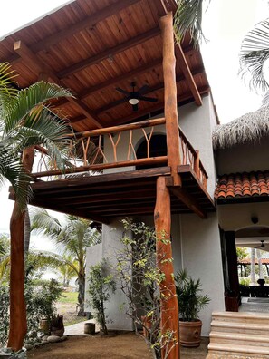 A wooden balcony with a thatched roof, surrounded by potted plants and palm trees. - Quaint 3-bedroom house with WiFi in Troncones (Troncones)