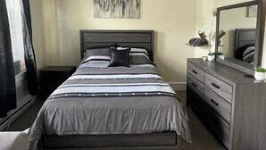 A bedroom with a bed, a dresser, a ceiling fan, a window with curtains, and a wall-mounted mirror.