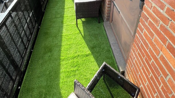 A balcony with artificial green turf, wicker furniture, and a brick wall.