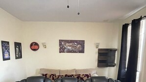 A room with a black leather sofa, a ceiling fan, wall art, and a window with curtains.