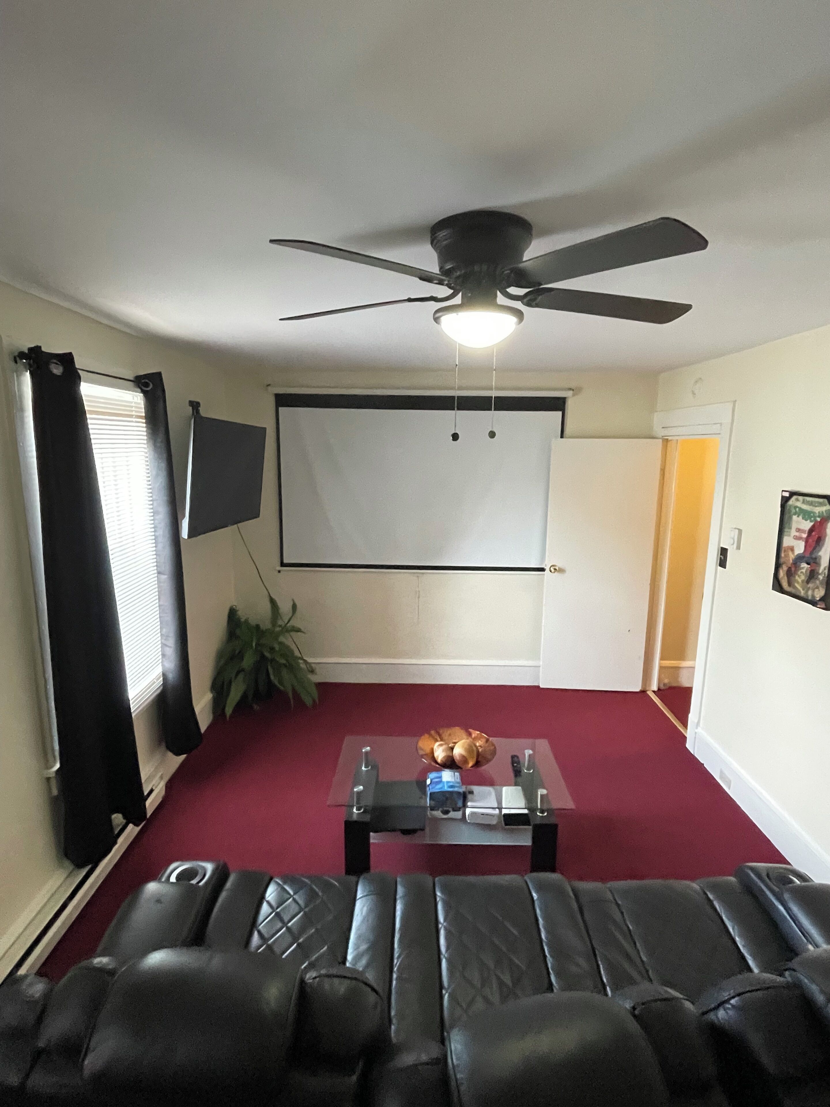 A living room with a ceiling fan, a projector screen, a coffee table, and a red carpet.