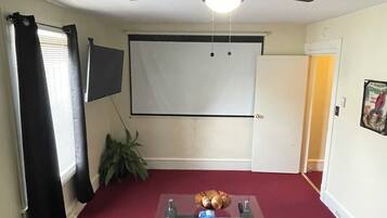 A living room with a ceiling fan, a projector screen, a coffee table, and a red carpet.