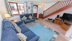 A living room with a sofa set, a television, a wooden cabinet, and a staircase. - Cockleshell Croyde | Sleeps 4 | By the Seaside (Croyde)