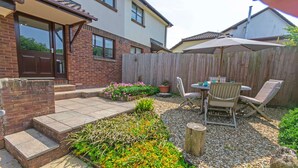 A backyard with a patio, a wooden fence, a table with chairs, and a potted plant. - Cockleshell Croyde | Sleeps 4 | By the Seaside (Croyde)