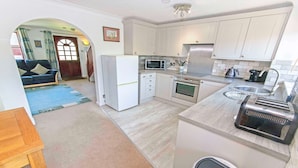 A compact kitchen with white cabinets, a microwave, an oven, a toaster, and a sink. - Cockleshell Croyde | Sleeps 4 | By the Seaside (Croyde)