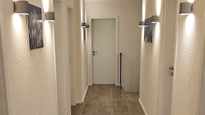 Un pasillo con suelo de madera, paredes blancas y puertas a ambos lados.