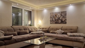Una sala moderna con un sofá seccional, una mesa de centro de vidrio y un cuadro floral en la pared.