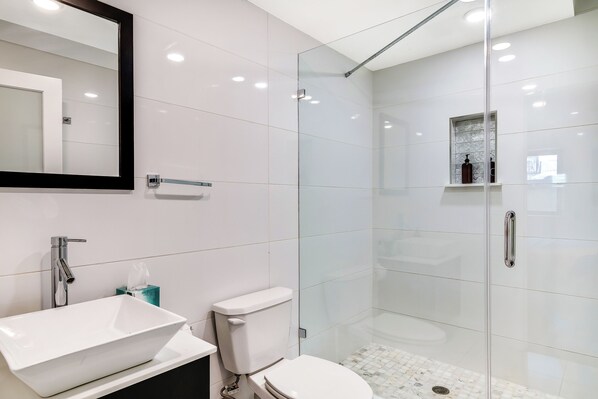 Un baño moderno con ducha de vidrio, lavamanos blanco y retrete.