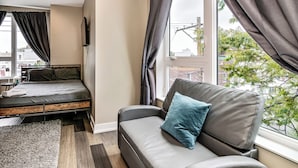 Habitación de hotel compacta con cama, sofá y ventana grande con vistas a la ciudad.