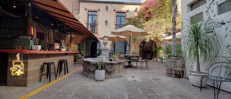 Un área de café al aire libre con suelo de piedra, mesas con sombrillas y plantas en macetas.