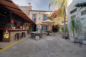 An outdoor café area with stone flooring, tables with umbrellas, and potted plants.