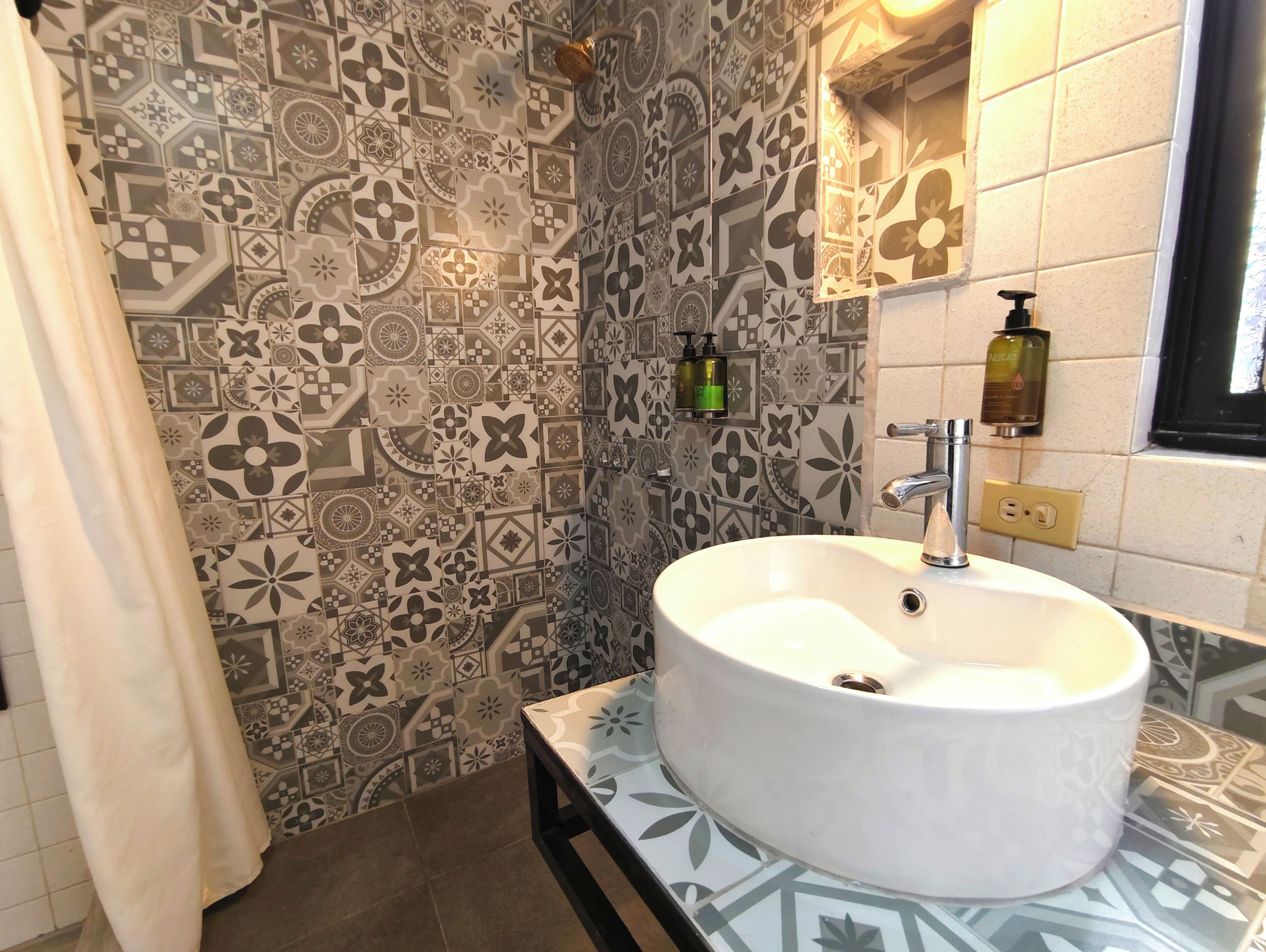Une salle de bain avec un lavabo blanc, des carreaux décorés, un rideau de douche et des articles de toilette accrochés au mur.