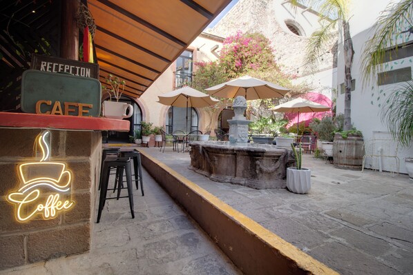 A cafe with a reception area, outdoor seating, and a fountain.