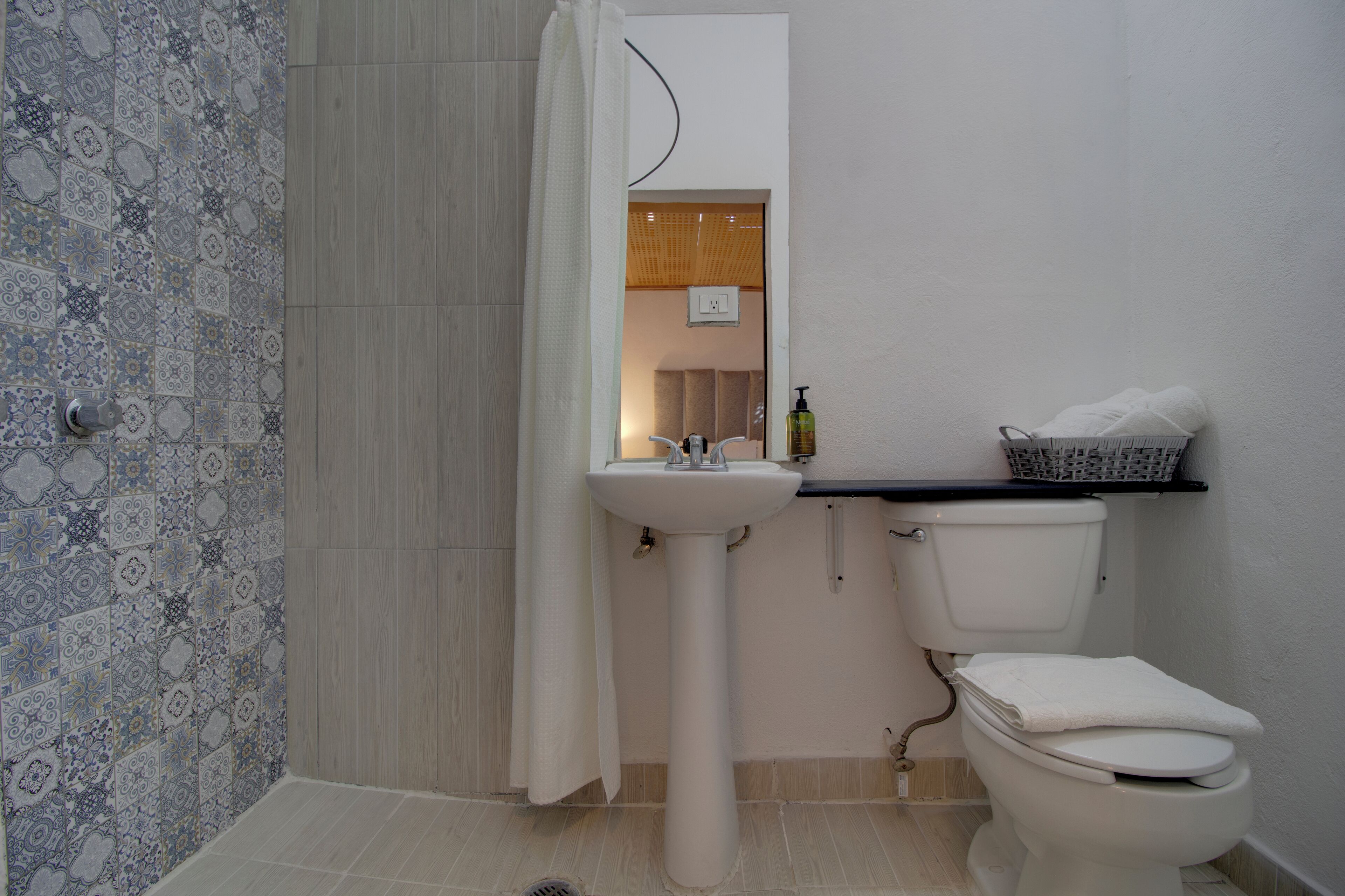 Een badkamer met een betegelde douche, een wastafel, een toilet en een klein plankje met toiletartikelen.