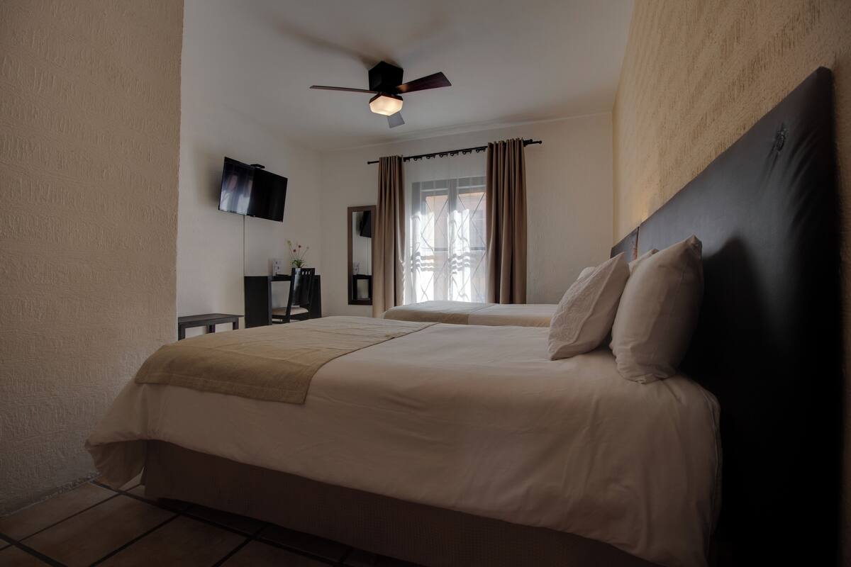Une chambre d’hôtel avec un grand lit, un ventilateur de plafond, un téléviseur à écran plat et une fenêtre avec des rideaux.