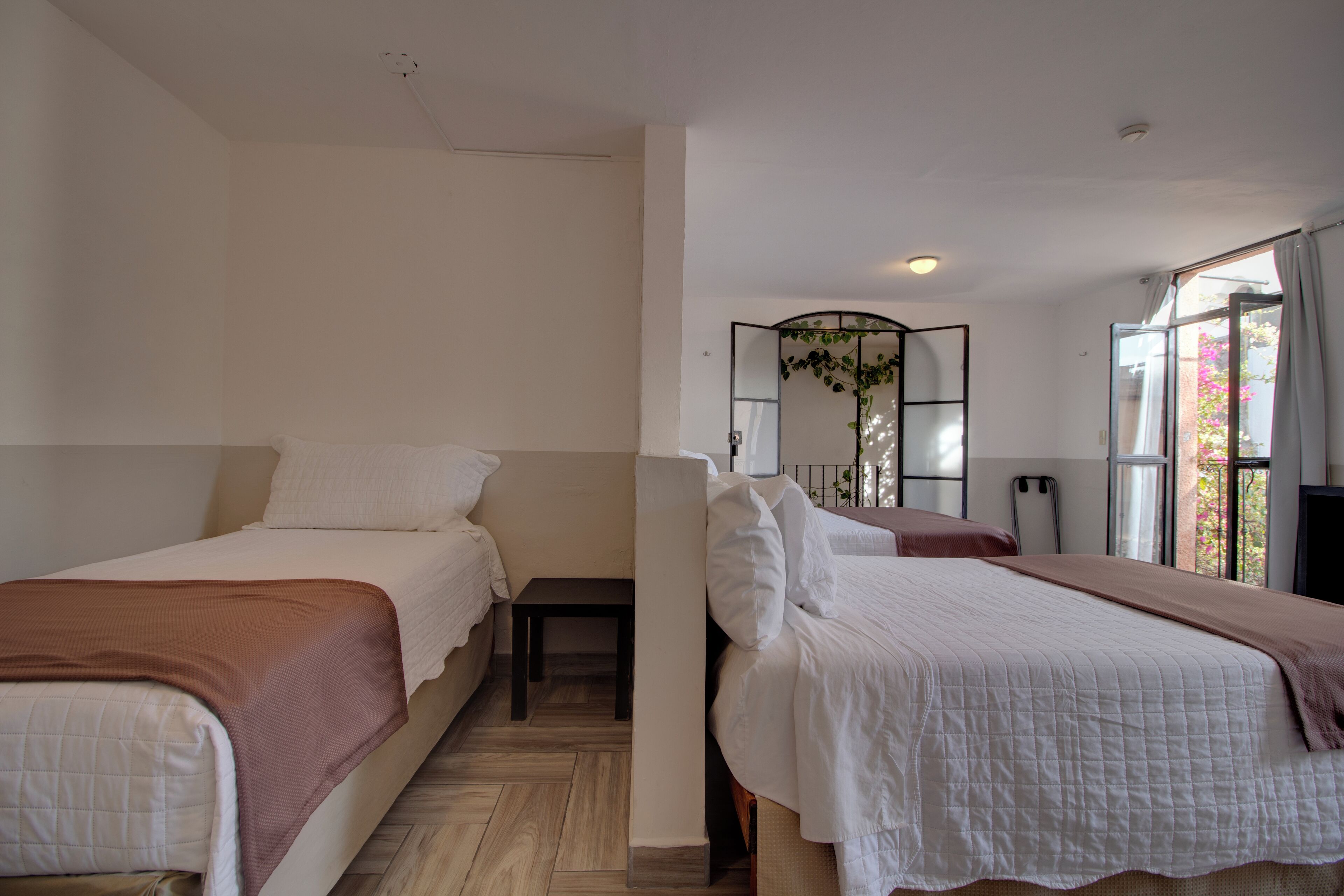 Habitación de hotel con dos camas, una mesita, un espejo y una ventana con vistas a zonas verdes.
