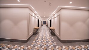 Un long couloir étroit, doté de carreaux de sol à motifs, de bancs en bois et d’un éclairage encastré.
