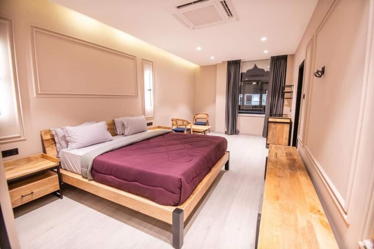 Une chambre moderne avec un lit en bois, des tables de chevet, un petit coin salon et une vue sur l’extérieur.
