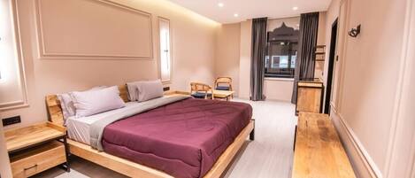 Un dormitorio moderno con cama de madera, mesitas de noche, un pequeño rincón de descanso y vistas al exterior.