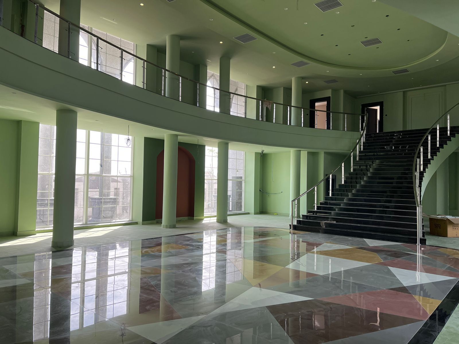 A spacious interior with a central staircase, large windows, and a geometric floor pattern.