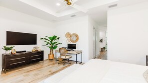 Une chambre moderne avec un grand lit, un bureau avec un ordinateur, une télévision et une grande plante.