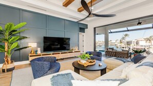 Ein modernes Wohnzimmer mit großem Fernseher, bequemen Sitzmöglichkeiten und Blick auf eine Marina.