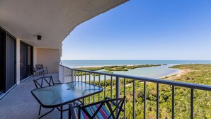 A balcony with a glass table and chairs, overlooking a coastal landscape with a clear view of the sea and a mangrove area. - Beachfront Bliss: A Perfect Getaway. (Marco Island)