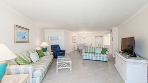 A spacious living room with a sofa, armchair, and a television. - Beachfront Bliss: A Perfect Getaway. (Marco Island)