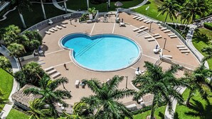 An aerial view of a resort with a large circular pool, palm trees, and lounge areas. - Beachfront Bliss: A Perfect Getaway. (Marco Island)