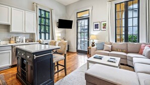 A spacious living room with a large sofa, a coffee table, and a kitchen area with a dining table and chairs. - The Retreat off Magazine (New Orleans)