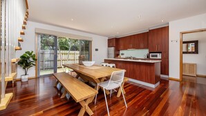 Une cuisine moderne avec des meubles en bois, un îlot central et un coin repas comprenant une table en bois et des chaises blanches.