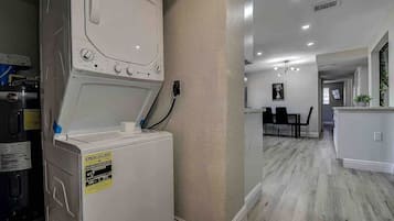 A laundry room with a front-loading washer and dryer, a dining area with a table and chairs, and a kitchen area with a countertop and sink.