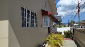 Un edificio residencial con techo rojo, una ventana con barrotes blancos y una planta en maceta al frente.