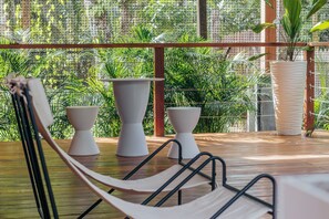 A hammock chair, two white planters, and a large potted plant on a wooden deck with a view of lush greenery through a wire mesh. - S Boutique Hotel  (Bocas del Toro)