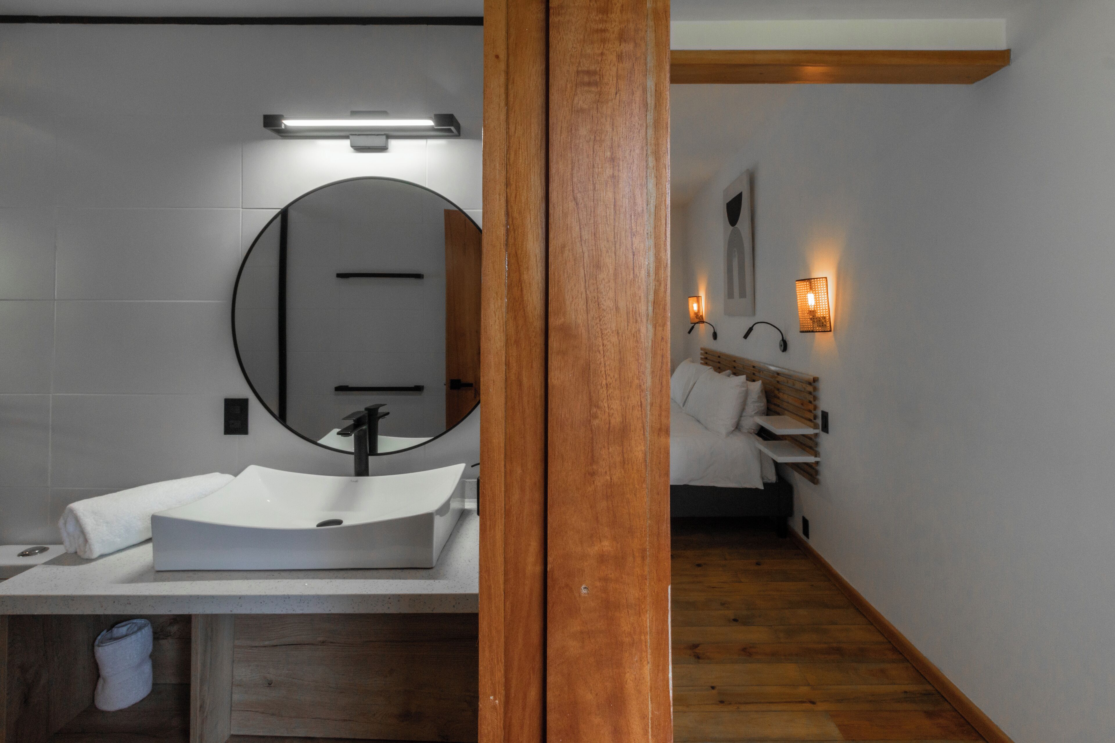 Een moderne badkamer met een ronde spiegel, een wit wastafelmeubel en houten details.