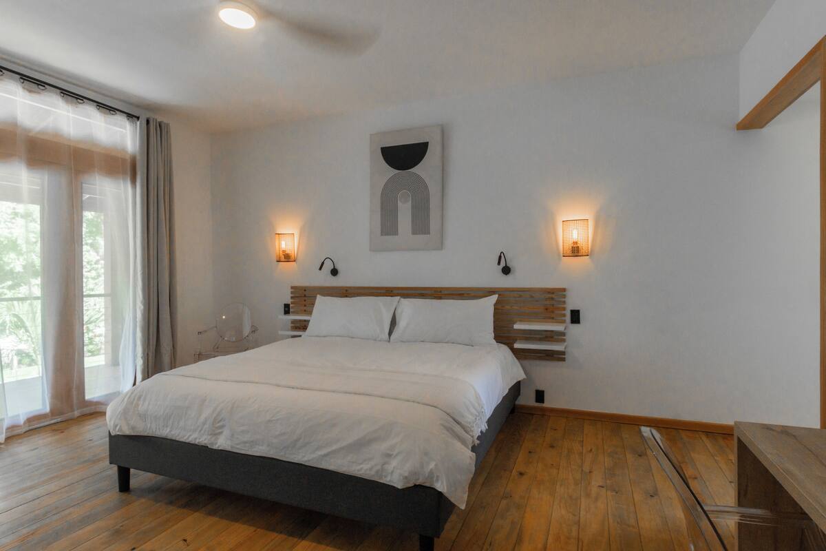 A bedroom with a large bed, wooden headboard, two bedside lamps, and a window with curtains.