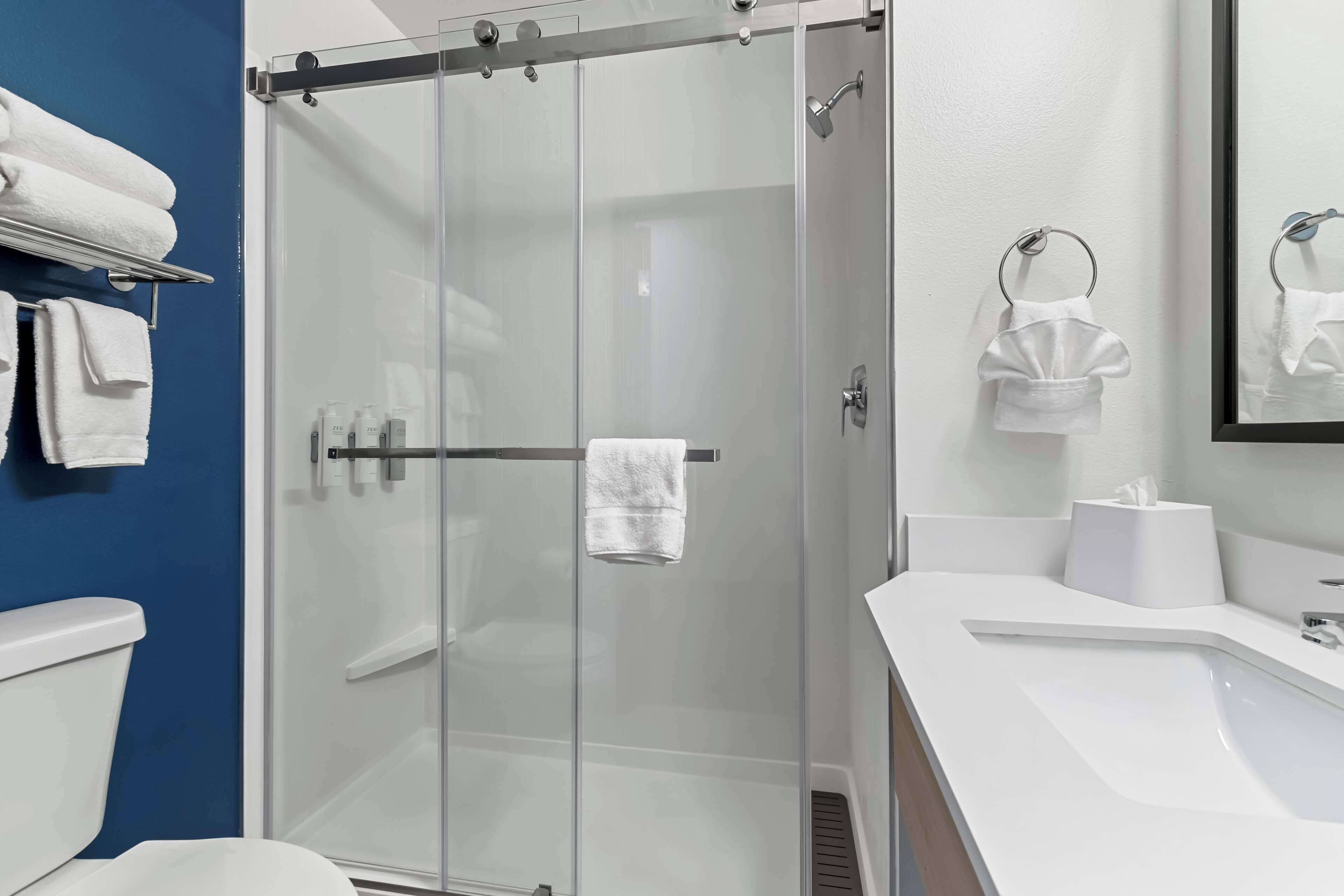 Une salle de bain moderne avec une douche à l’italienne en verre, des éléments d’ameublement blancs et un mur d’accent bleu.