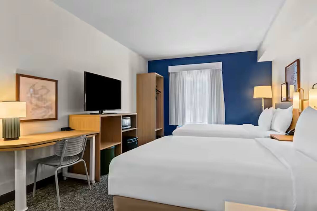 A hotel room with two beds, a desk with a chair, a television, a wardrobe, and a window with curtains.