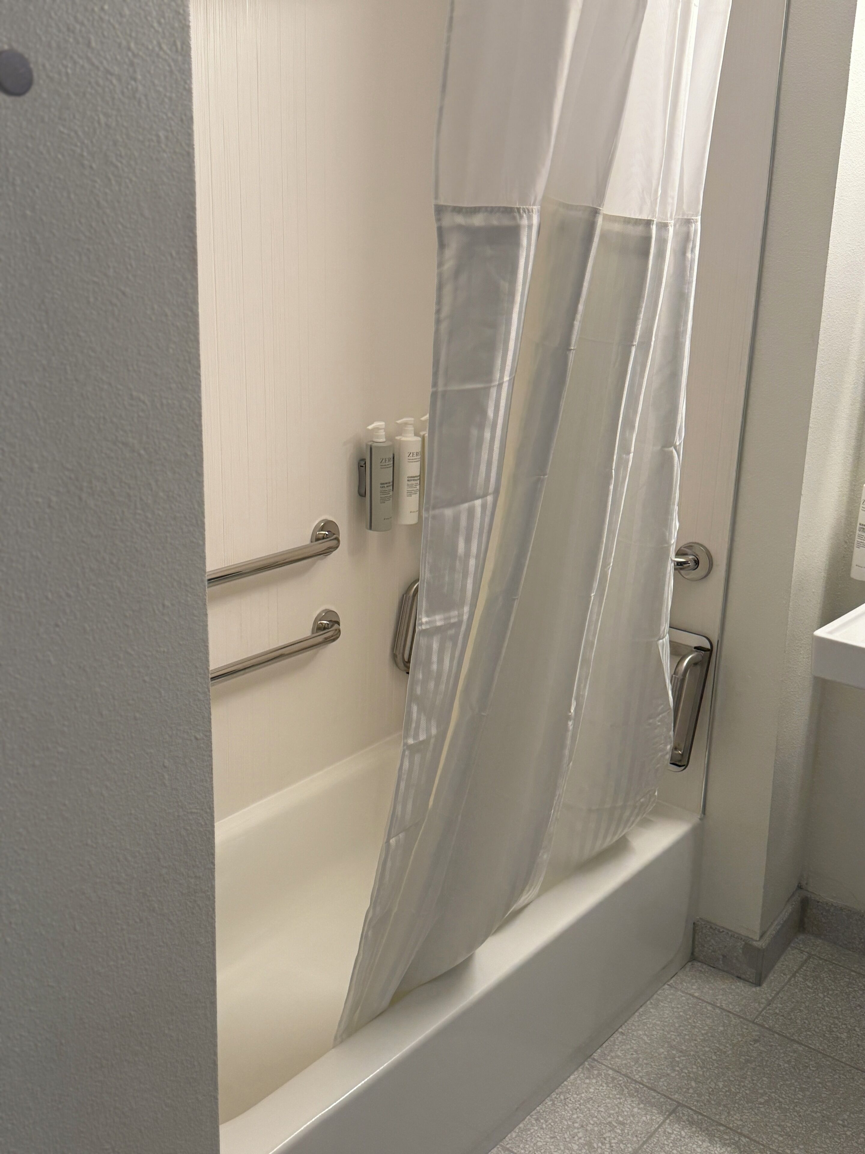Un baño con bañera, cortina de ducha y barra de apoyo.