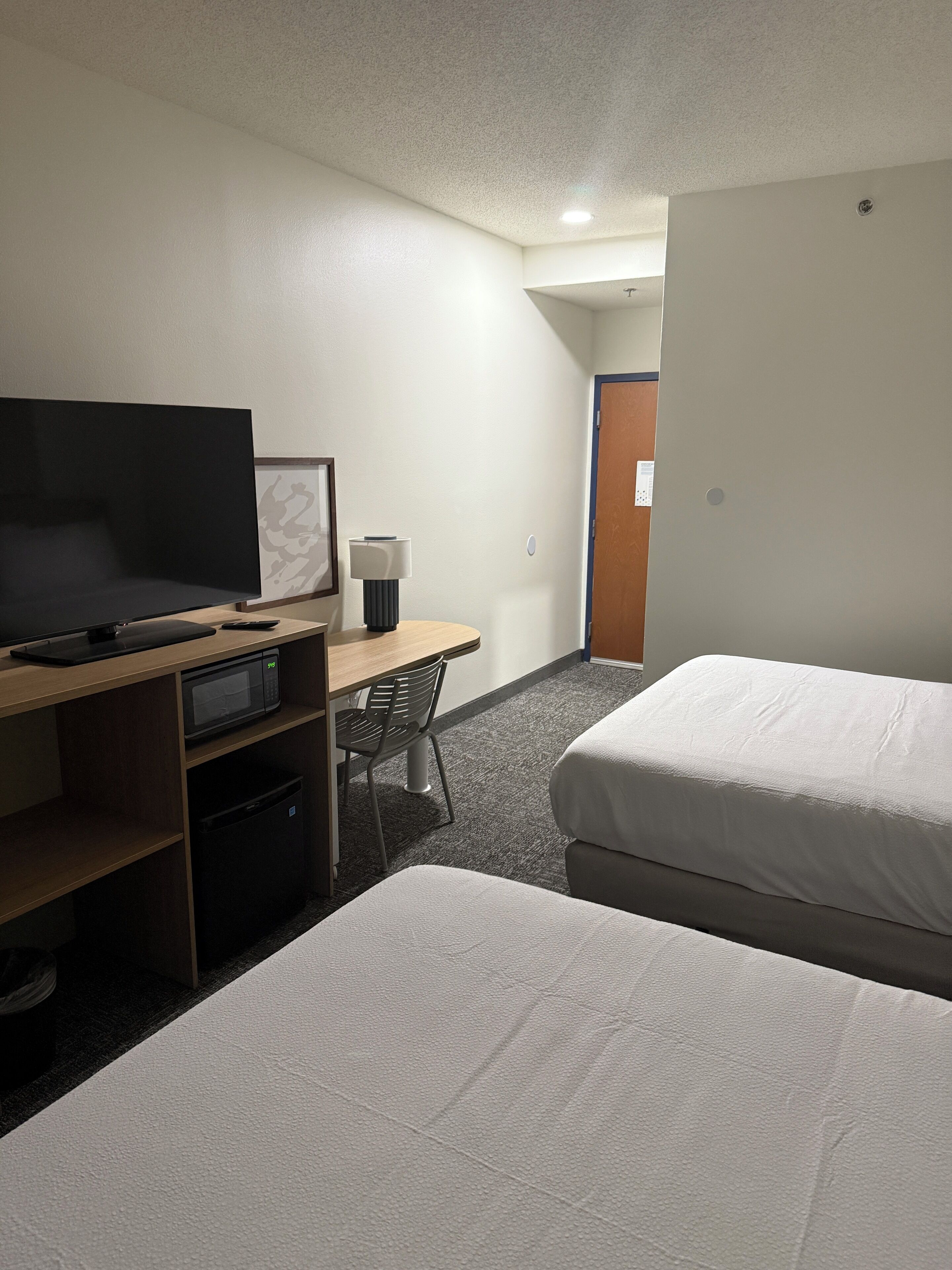 Ein Hotelzimmer mit Flachbildfernseher, Schreibtisch mit Lampe, Mikrowelle und zwei Betten.