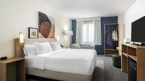 A hotel room with a large bed, a desk, a wardrobe, a television, and a window with curtains.
