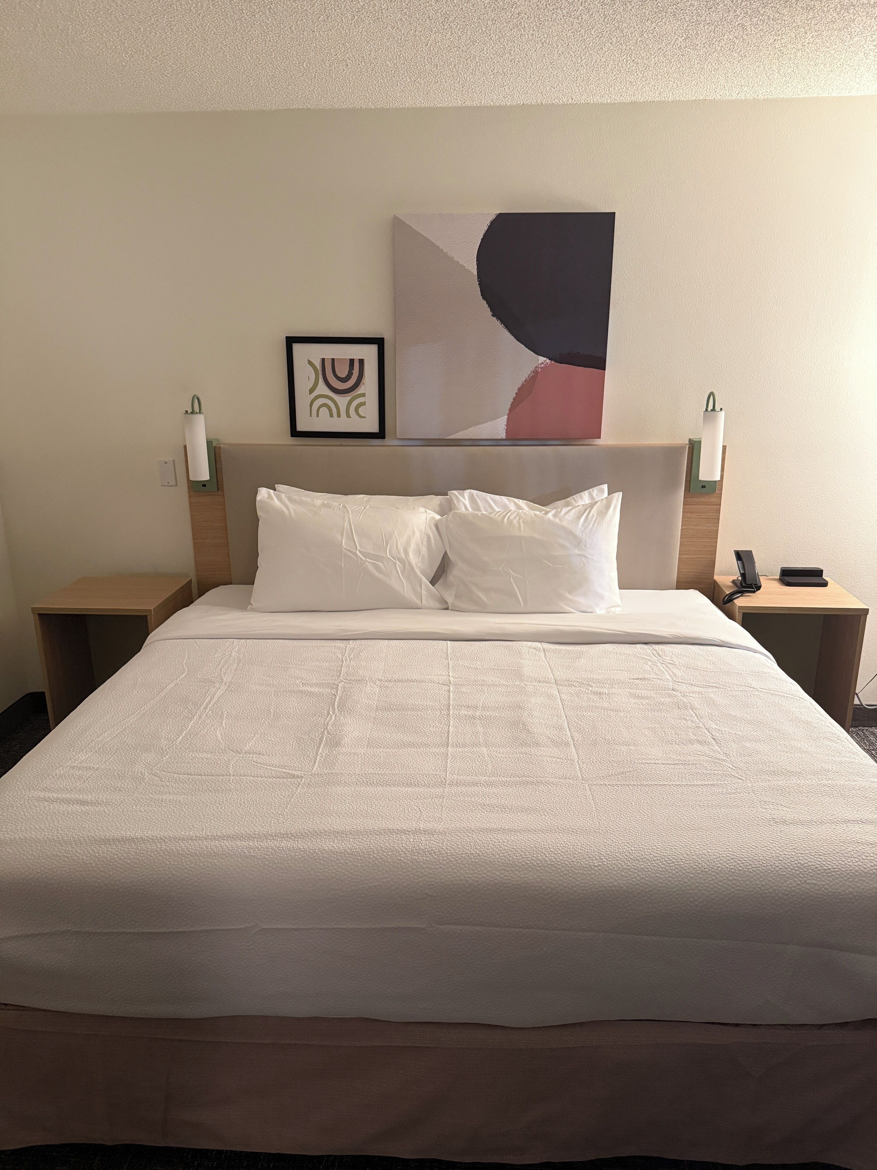 A neatly made bed with white linens, a headboard with a painting, and two bedside lamps on wooden nightstands.