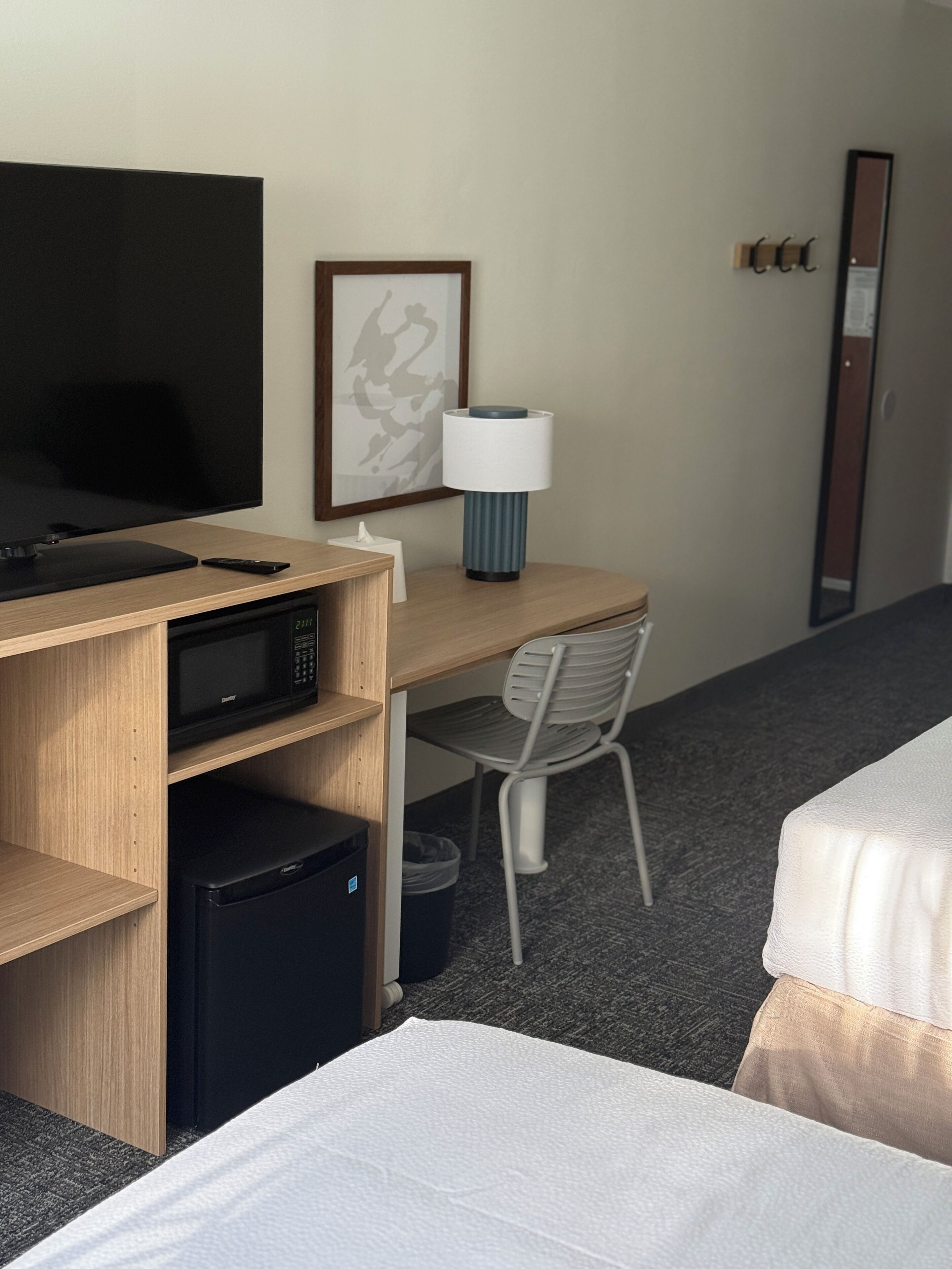 A hotel room with a bed, a desk with a lamp, a television, a microwave, and a trash bin.