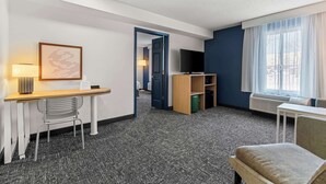 Habitación de hotel con escritorio, silla, televisión y ventana con cortinas.