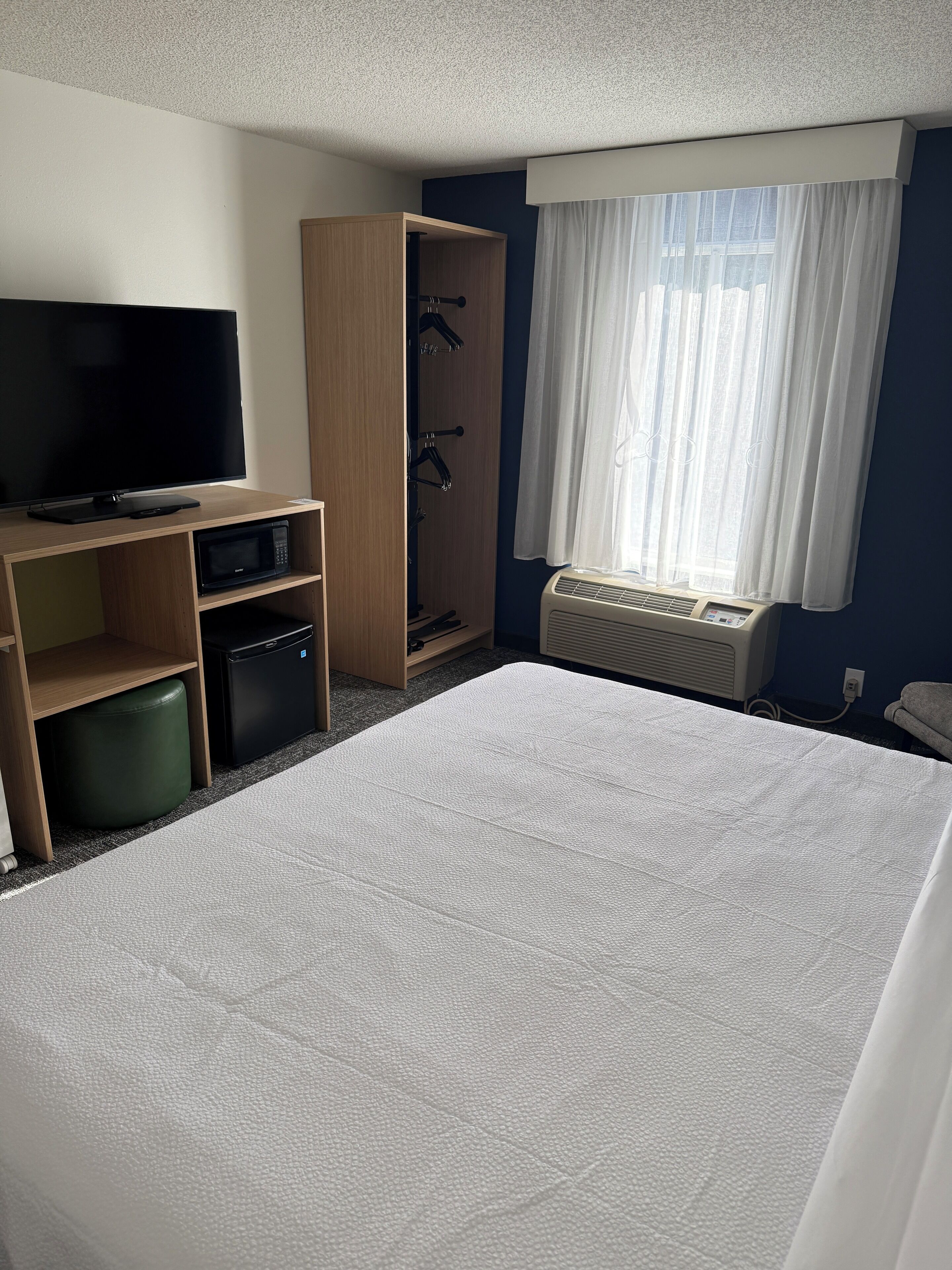 Habitación de hotel con cama, televisión, microondas, refrigerador pequeño, armario y ventana con cortinas.