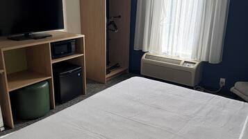 Habitación de hotel con cama, televisión, microondas, refrigerador pequeño, armario y ventana con cortinas.