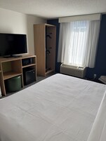 Habitación de hotel con cama, televisión, microondas, refrigerador pequeño, armario y ventana con cortinas.